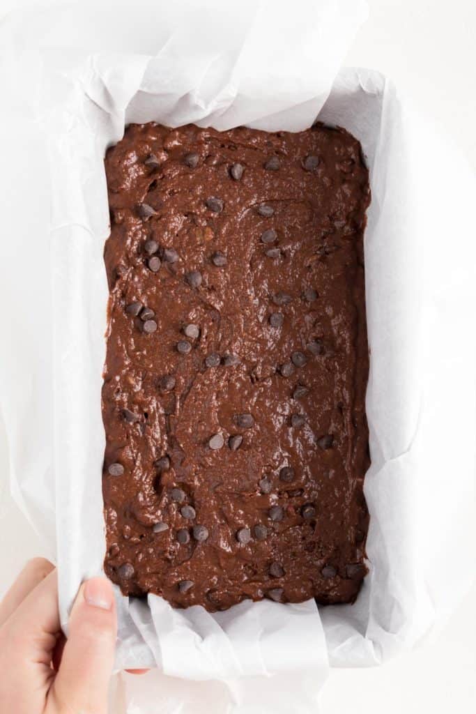 chocolate banana bread batter inside a loaf pan lined with parchment paper