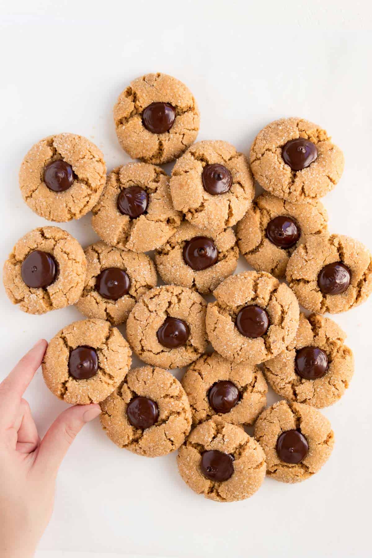 a hand grabbing a pile of vegan peanut butter blossoms on a white surface