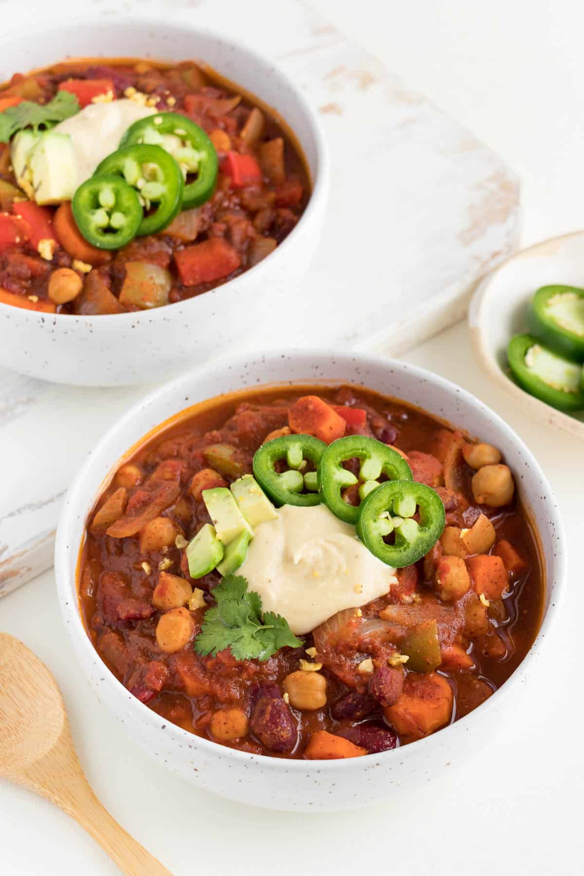 two white ceramic bowls filled with vegan three bean chili next to a wooden spoon