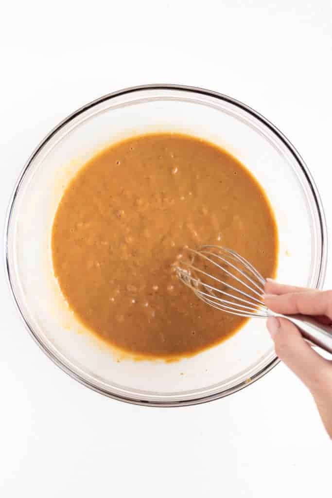 a wooden spoon mixing wet banana bars batter in a glass bowl