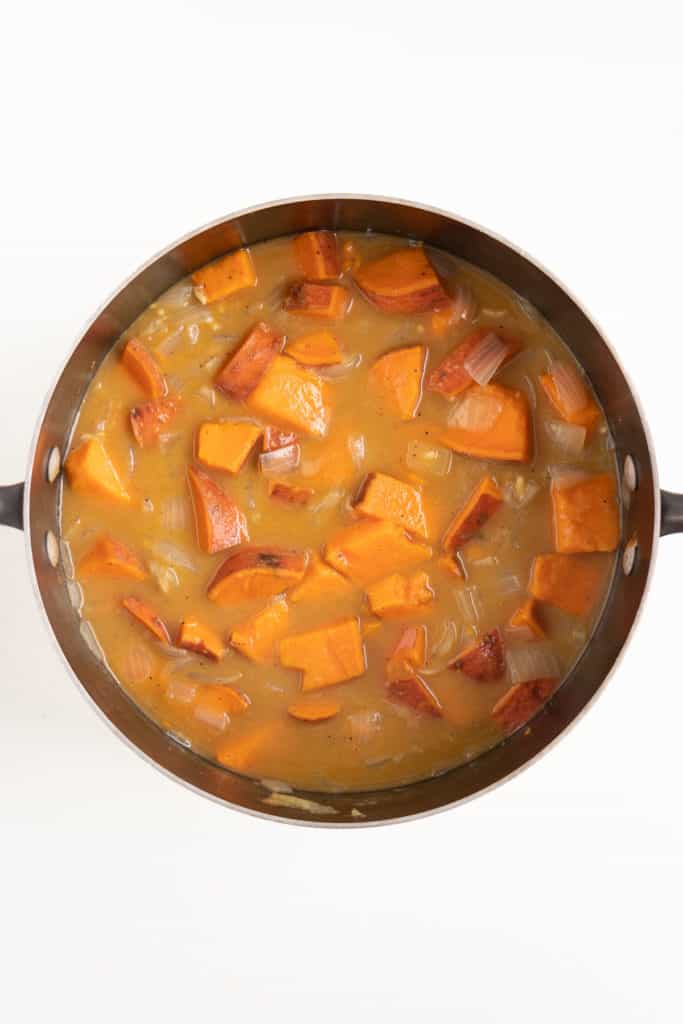vegetable broth and cubed sweet potatoes inside a black sauce pot