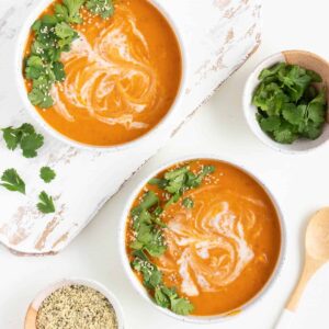 two bowls of creamy vegan sweet potato soup next to small bowls with cilantro and hemp seeds inside