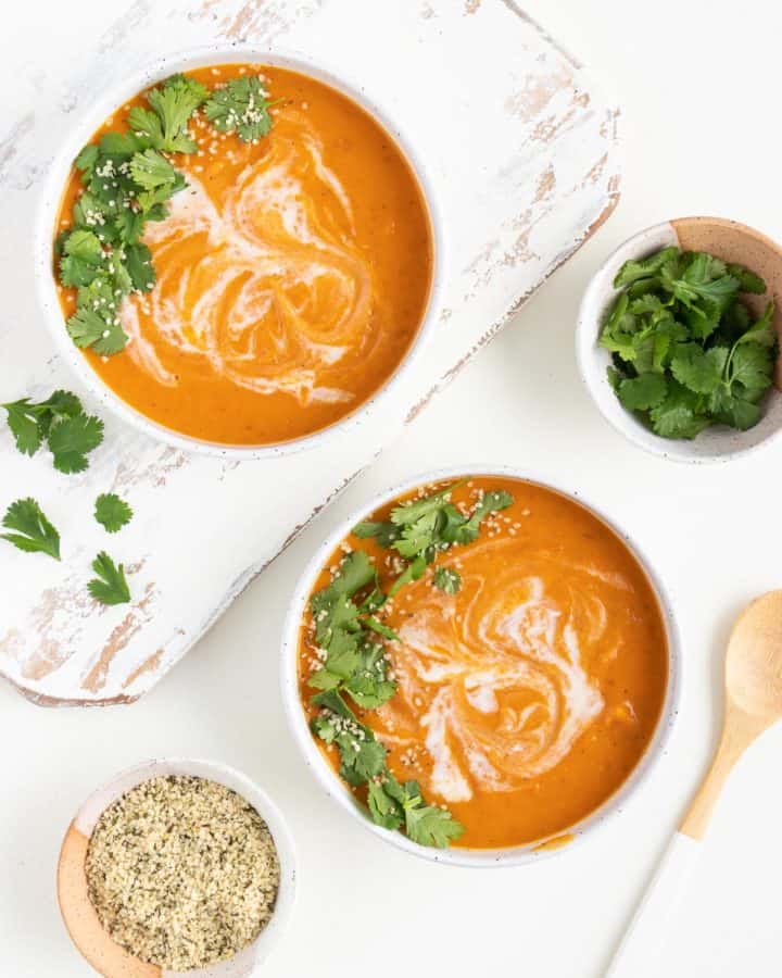 two bowls of creamy vegan sweet potato soup next to small bowls with cilantro and hemp seeds inside