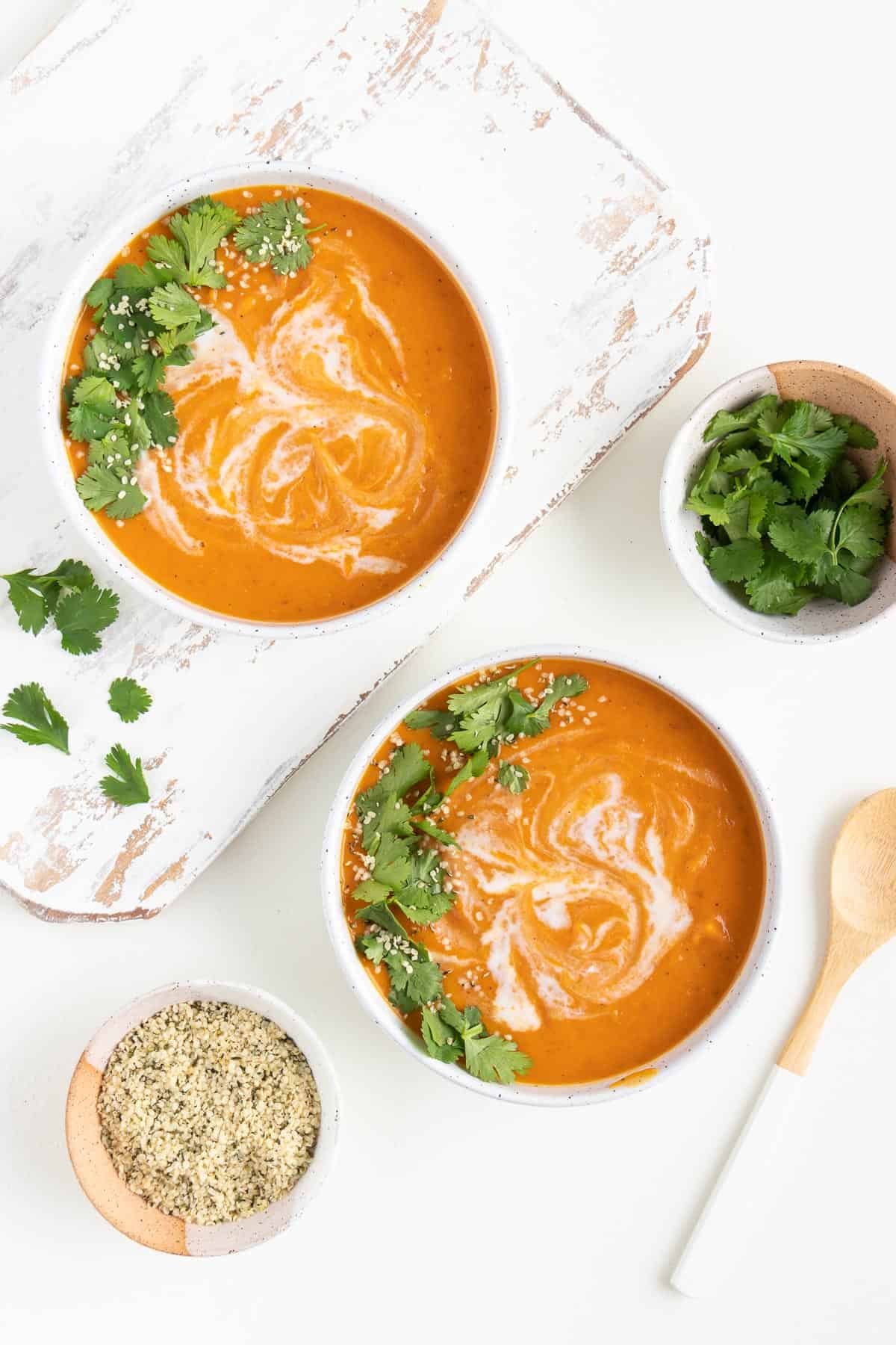 two bowls of creamy vegan sweet potato soup next to small bowls with cilantro and hemp seeds inside