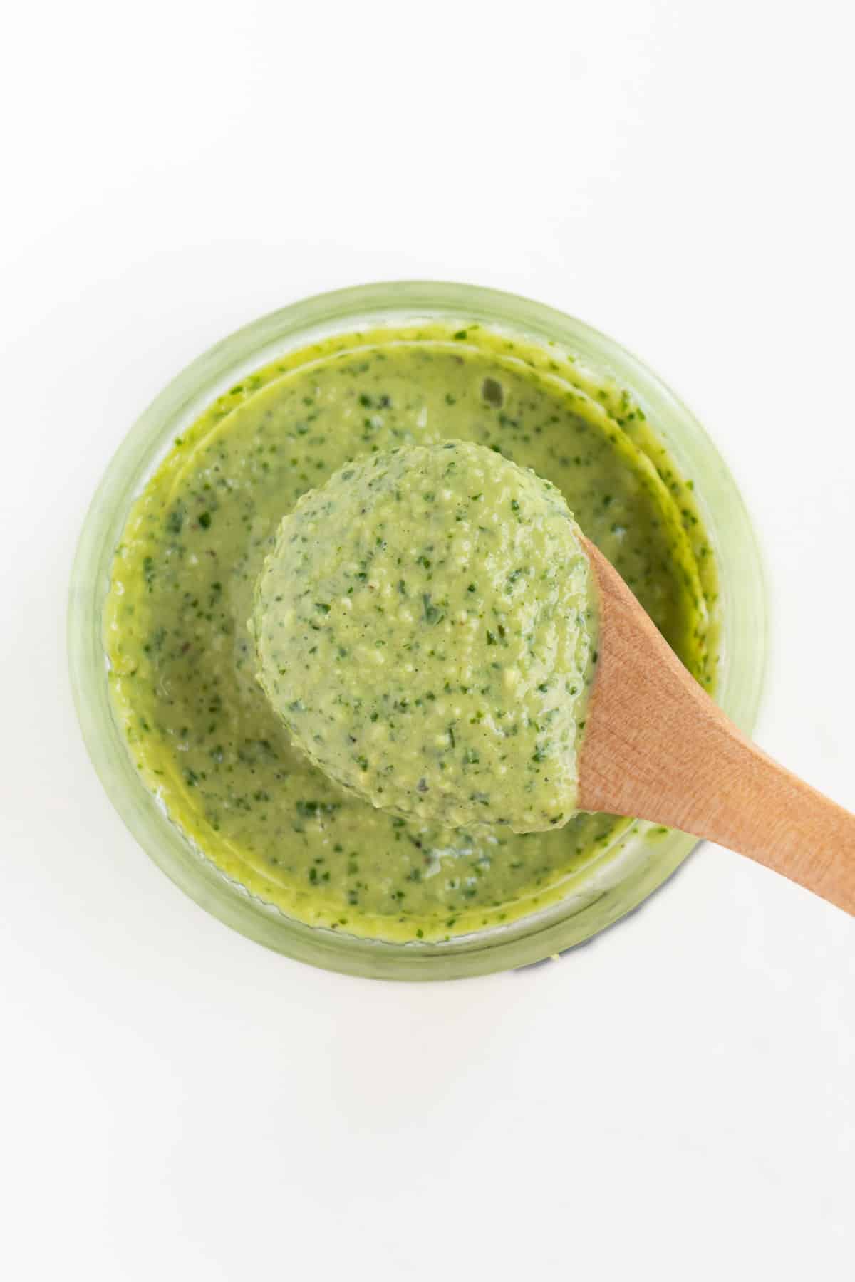 a wooden spoon scooping vegan pesto out of a glass jar