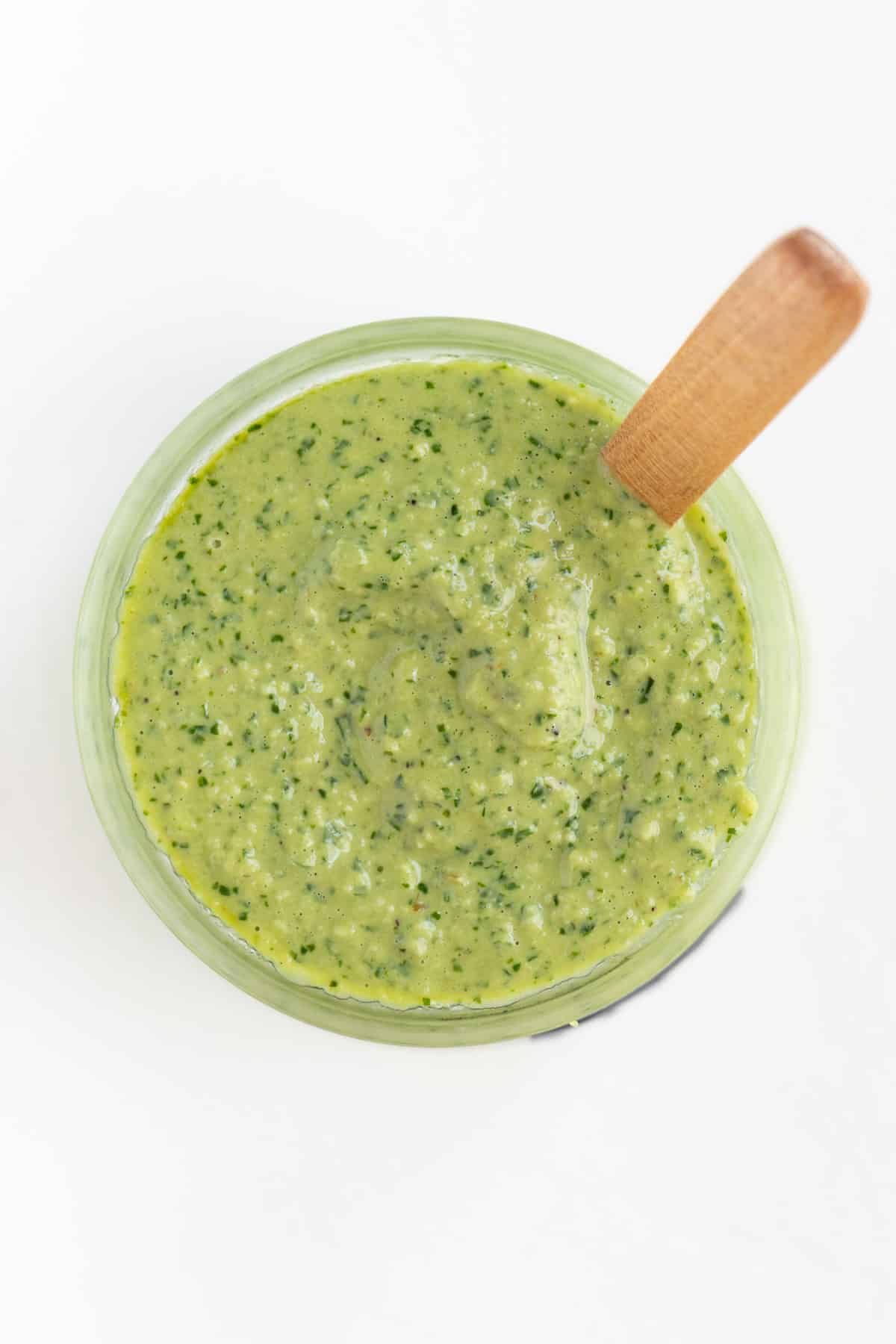 green pesto sauce inside a glass jar with a wooden spoon sticking out of it