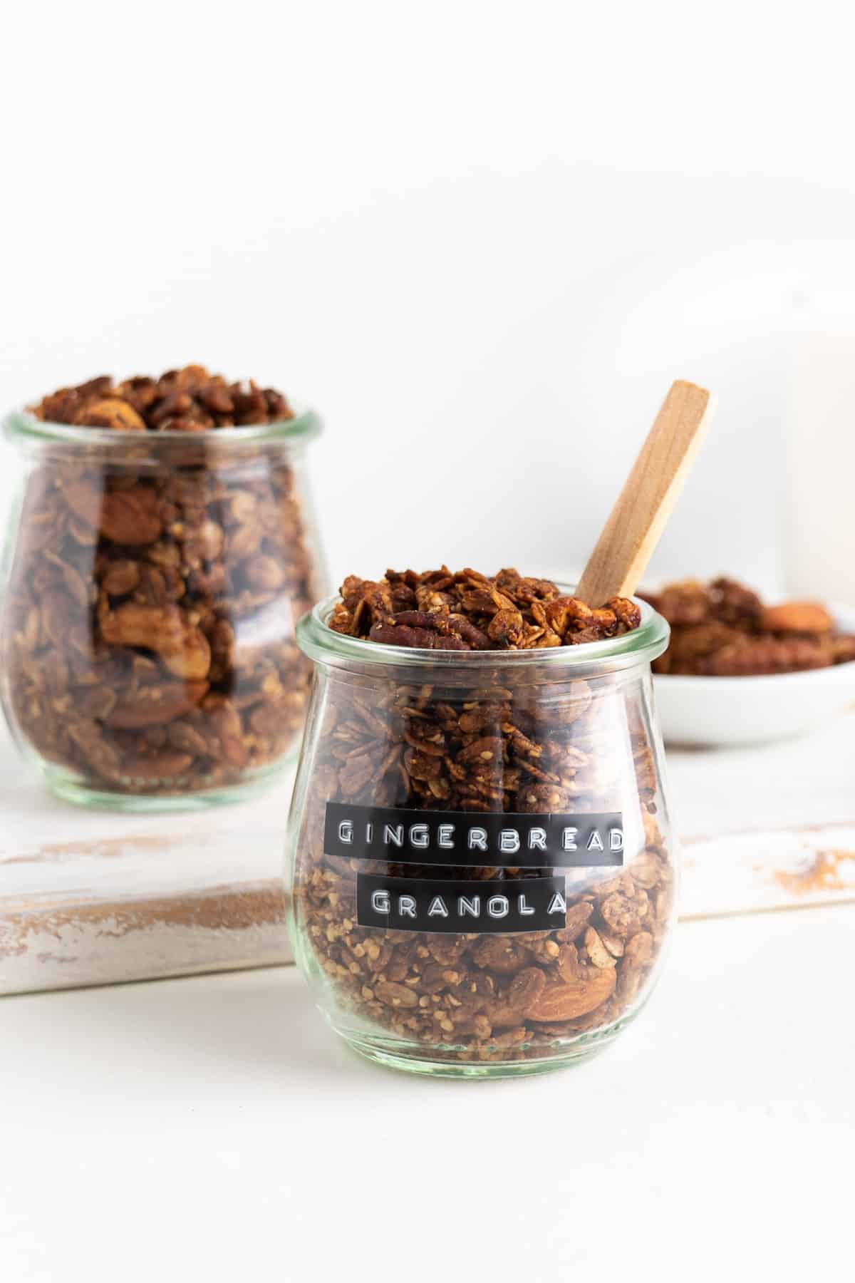 two glass jars filled with gingerbread granola on a distressed white wooden cutting board