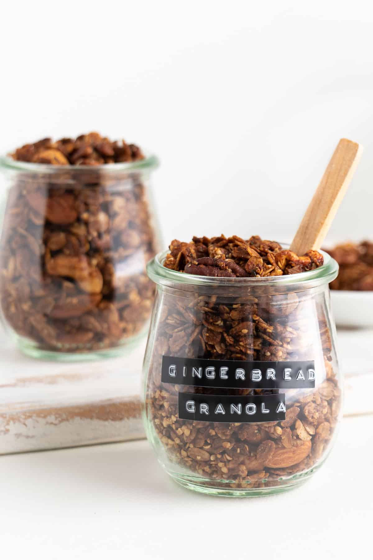 two glass jars filled with gingerbread granola on a white distressed cutting board
