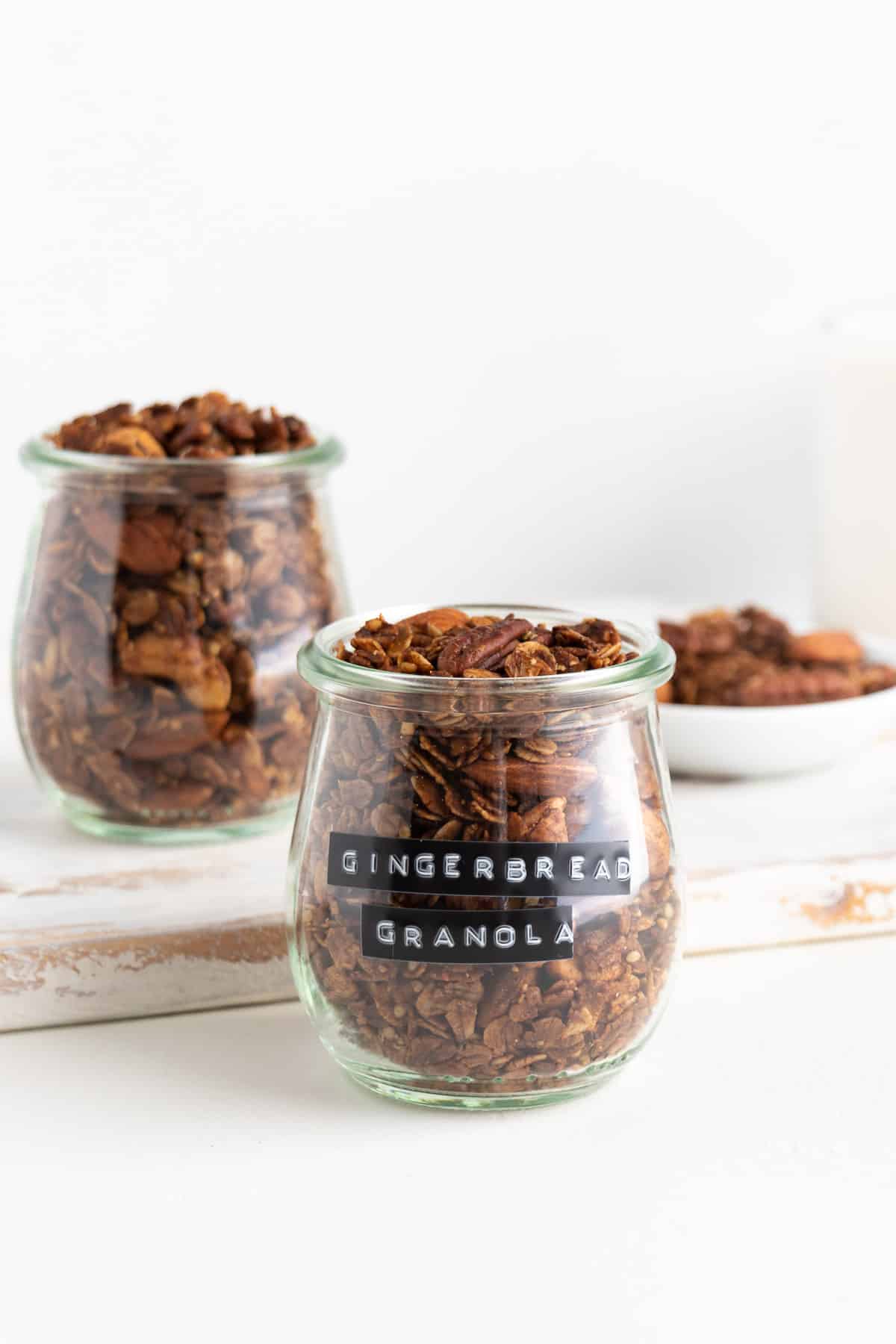 two glass jars filled with gingerbread granola on a white distressed cutting board