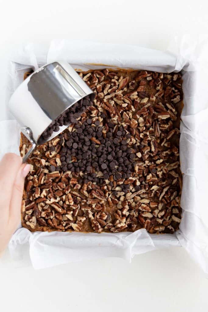 hand pouring a measuring cup of mini chocolate chips on top of a square baking dish