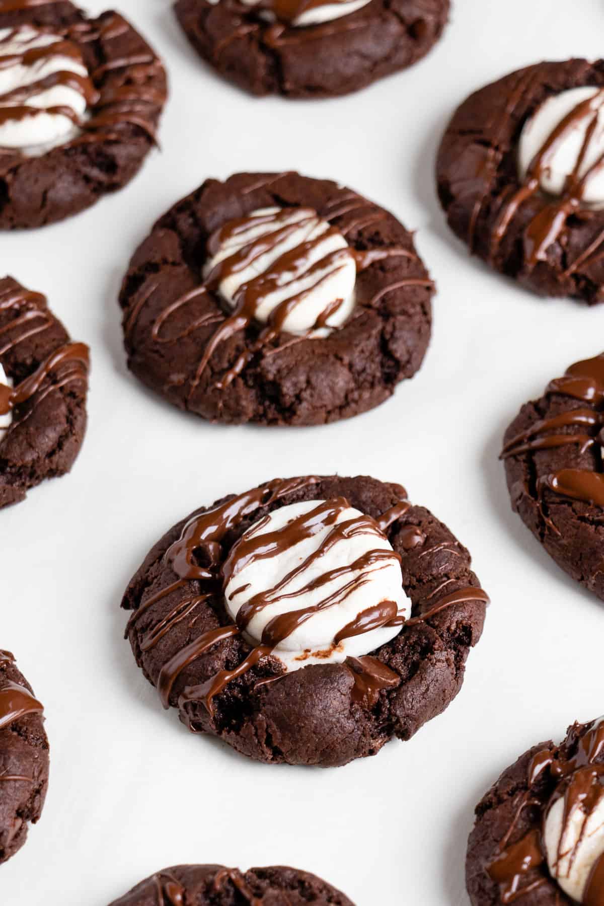 vegan hot cocoa cookies topped with marshmallows and a chocolate drizzle on a white surface