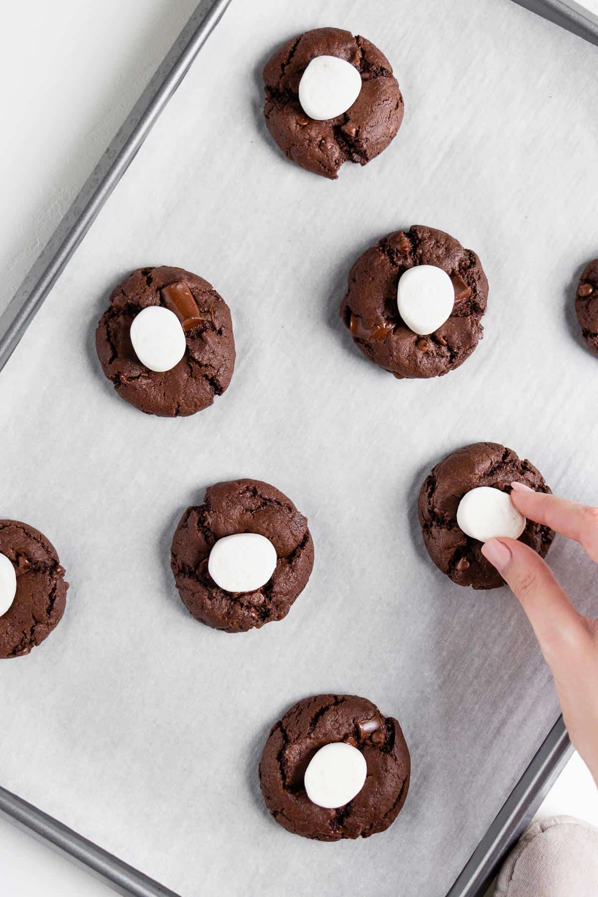 a hand pressing marshmallows on top of vegan double chocolate chunk cookies