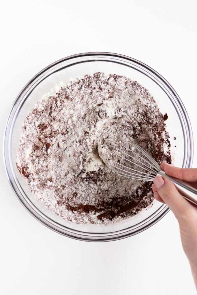 a hand whisking flour and cocoa powder together in a glass bowl