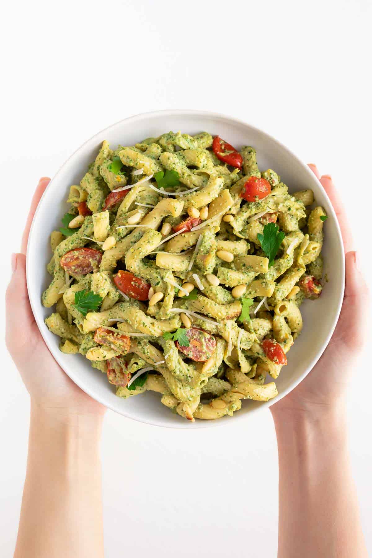 two hands holding a bowl of vegan pesto cavatappi pasta