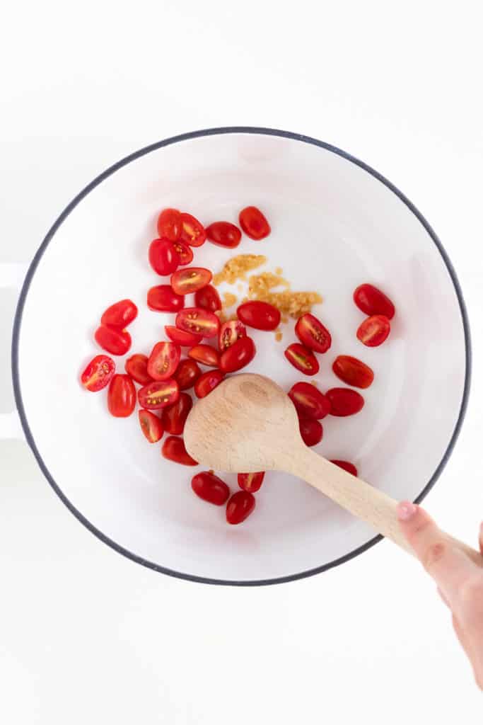 cherry tomatoes and minced garlic in a white sauce pot