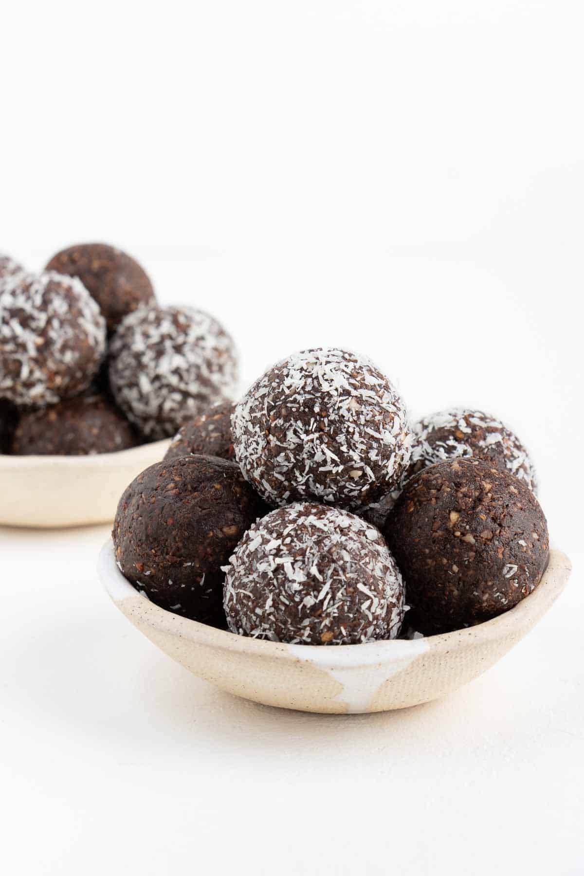 two stacks of coconut chocolate energy balls inside ceramic bowls