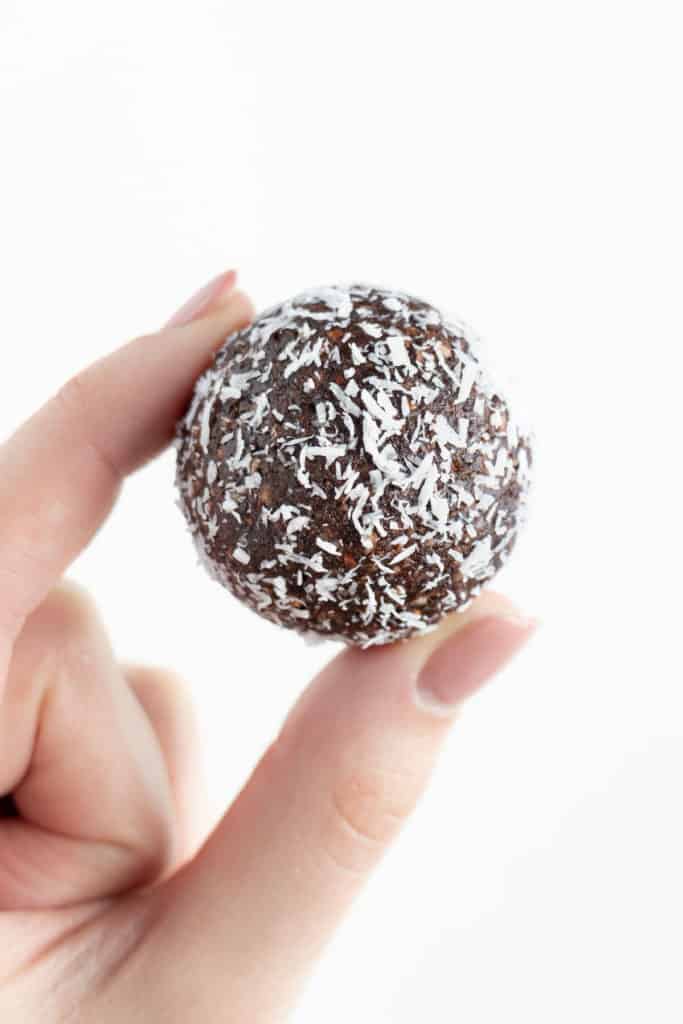 a hand holding a date ball covered in shredded coconut