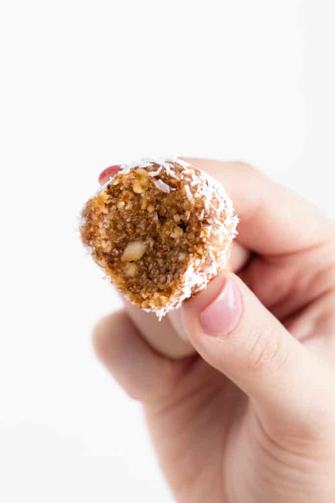 hand holding an almond coconut energy ball with a bite taken out of it