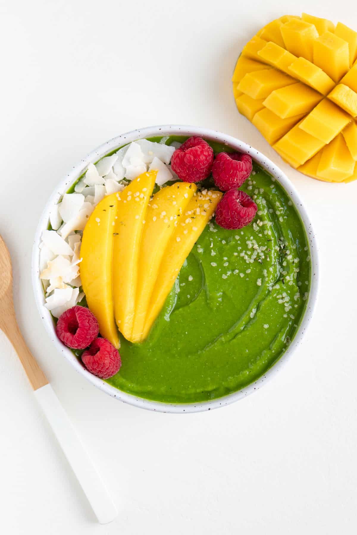 a bowl filled with a green smoothie and fresh fruit beside a wooden spoon