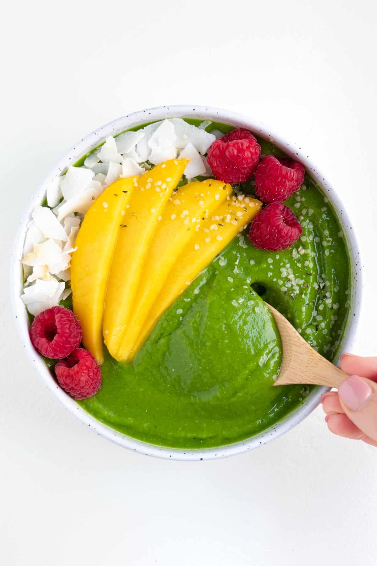 a hand holding a wooden spoon scooping a bite out of a smoothie bowl