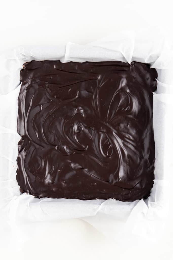 chocolate ganache swirled over raw vegan brownies in a square baking dish