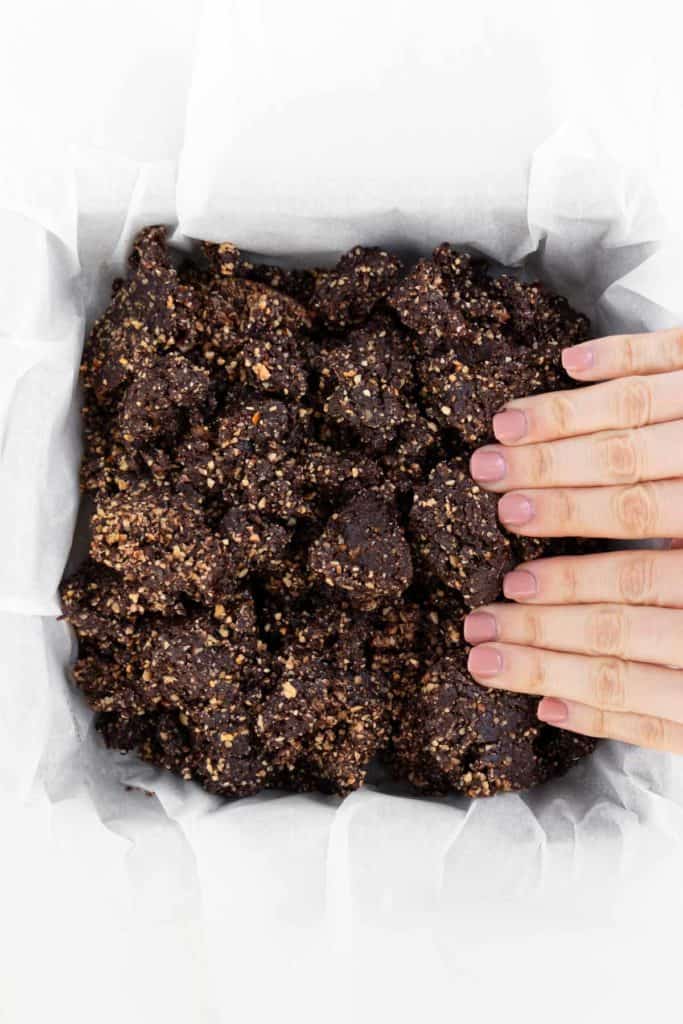 two hands pressing raw vegan brownie dough into a square baking dish