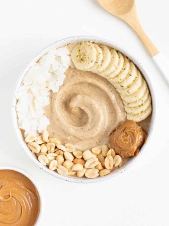 peanut butter banana smoothie bowl beside a bowl of peanut butter and a wooden spoon