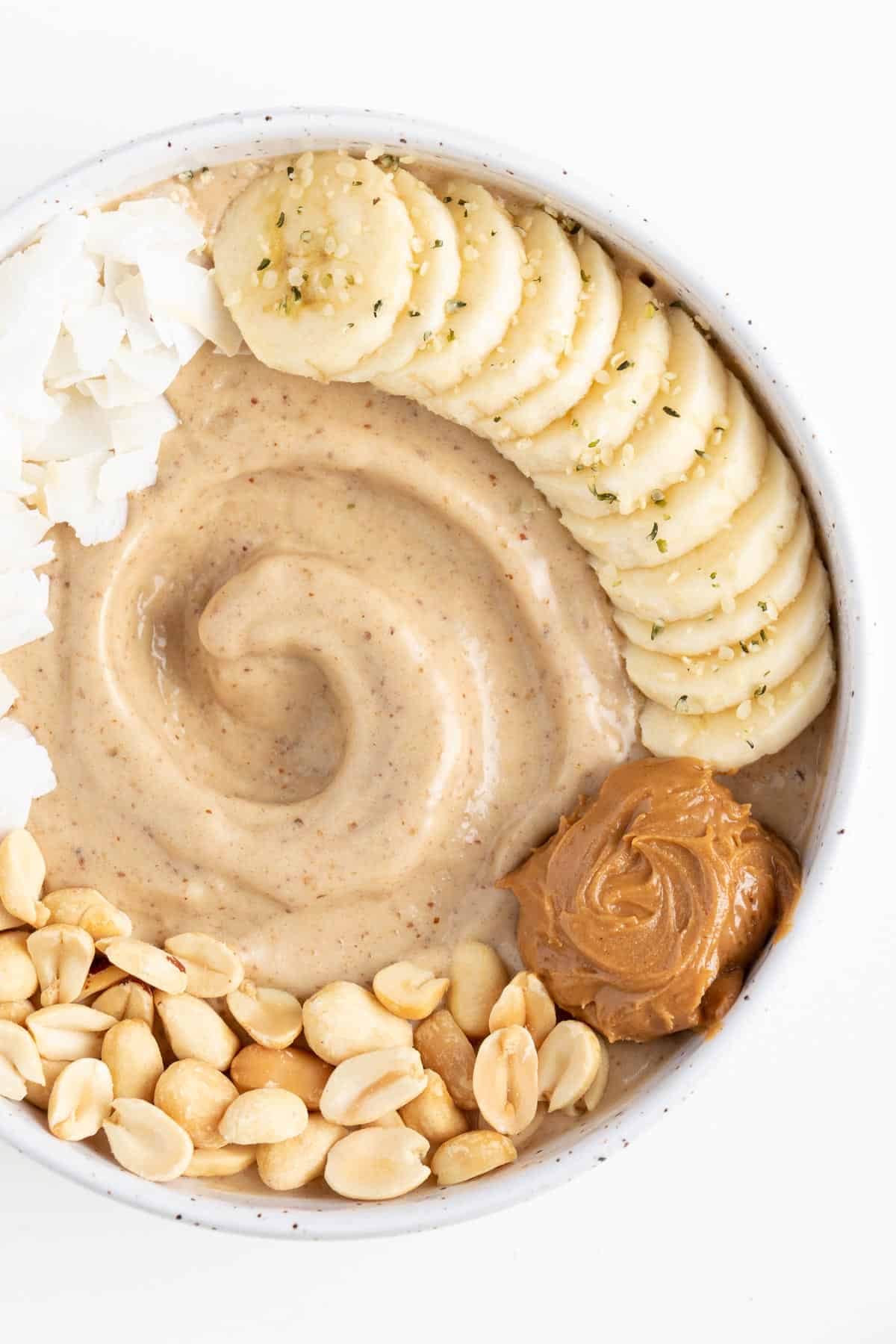 chopped nuts, coconut flakes, fruit, and nut butter on top of a bowl