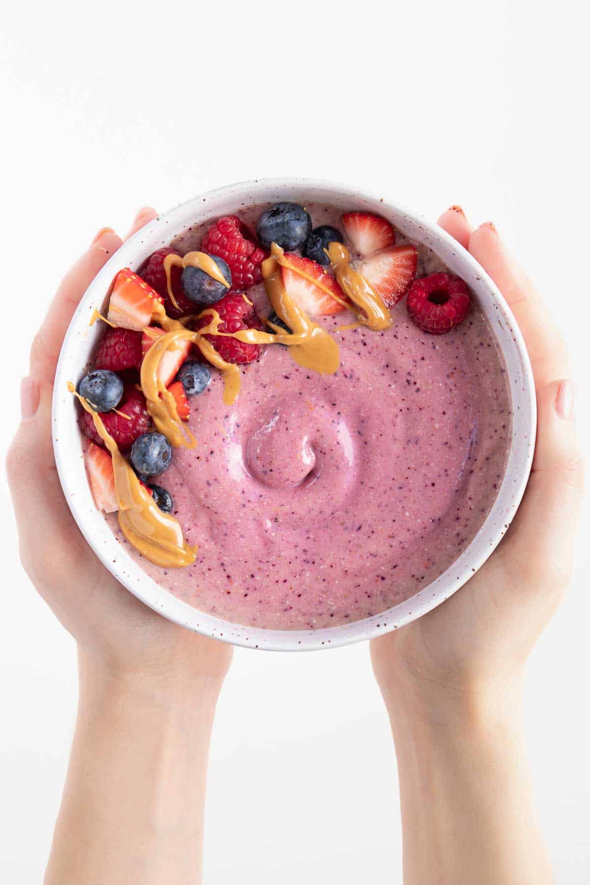 two hands holding a purple smoothie topped with blueberries, raspberries, and strawberries