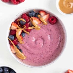 peanut butter and jelly smoothie bowl beside small bowls of berries and peanut butter