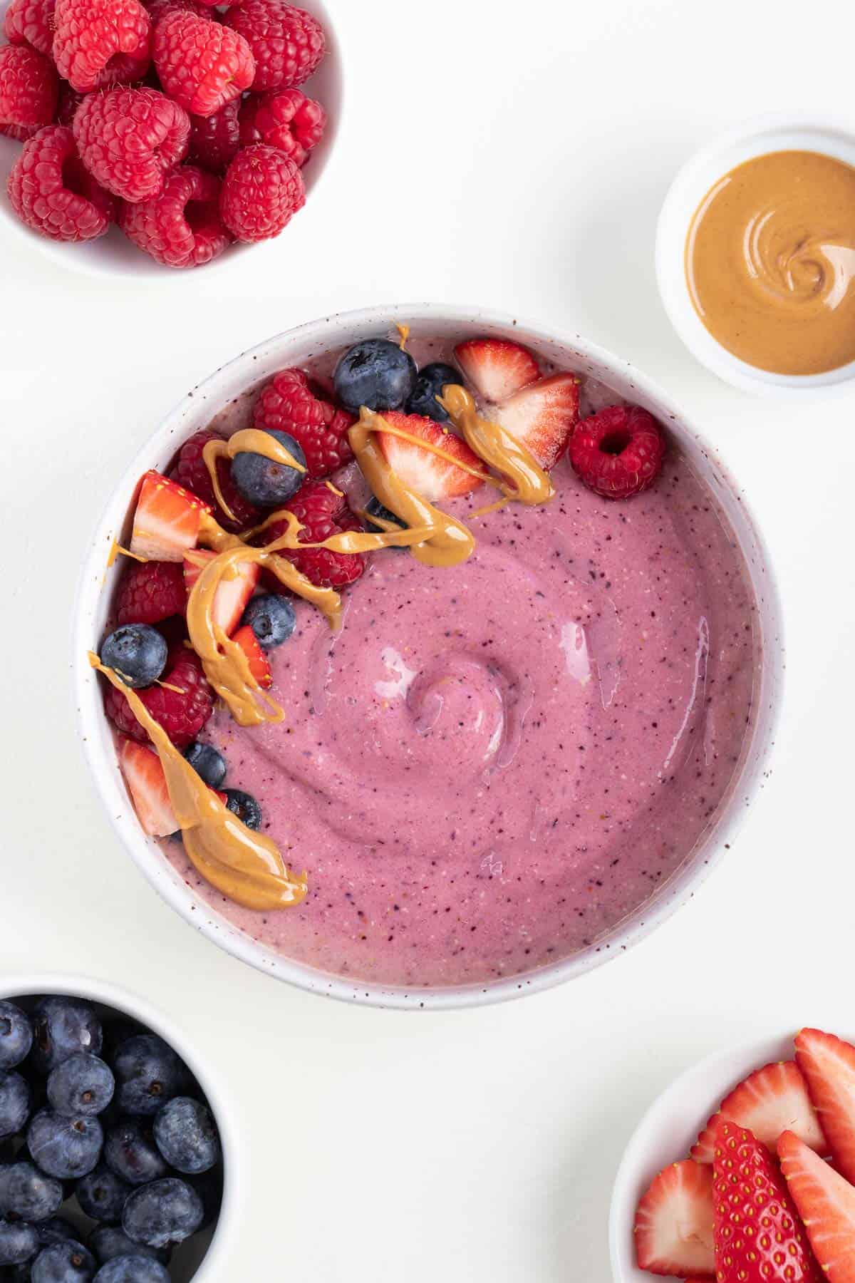 peanut butter and jelly smoothie bowl beside small bowls of berries and peanut butter