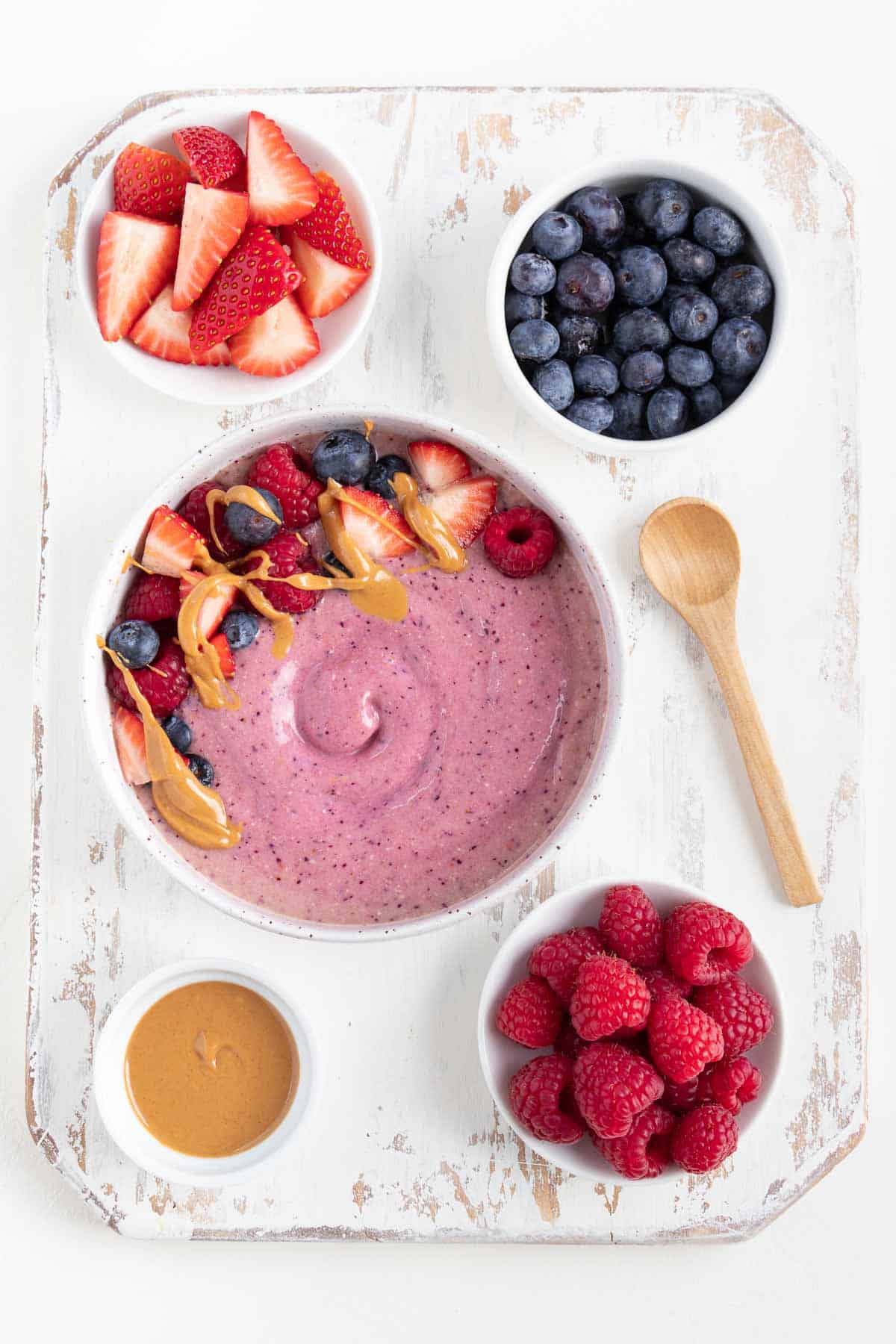 peanut butter and jelly smoothie bowl, a wooden spoon, and berries on top of a white distressed cutting board