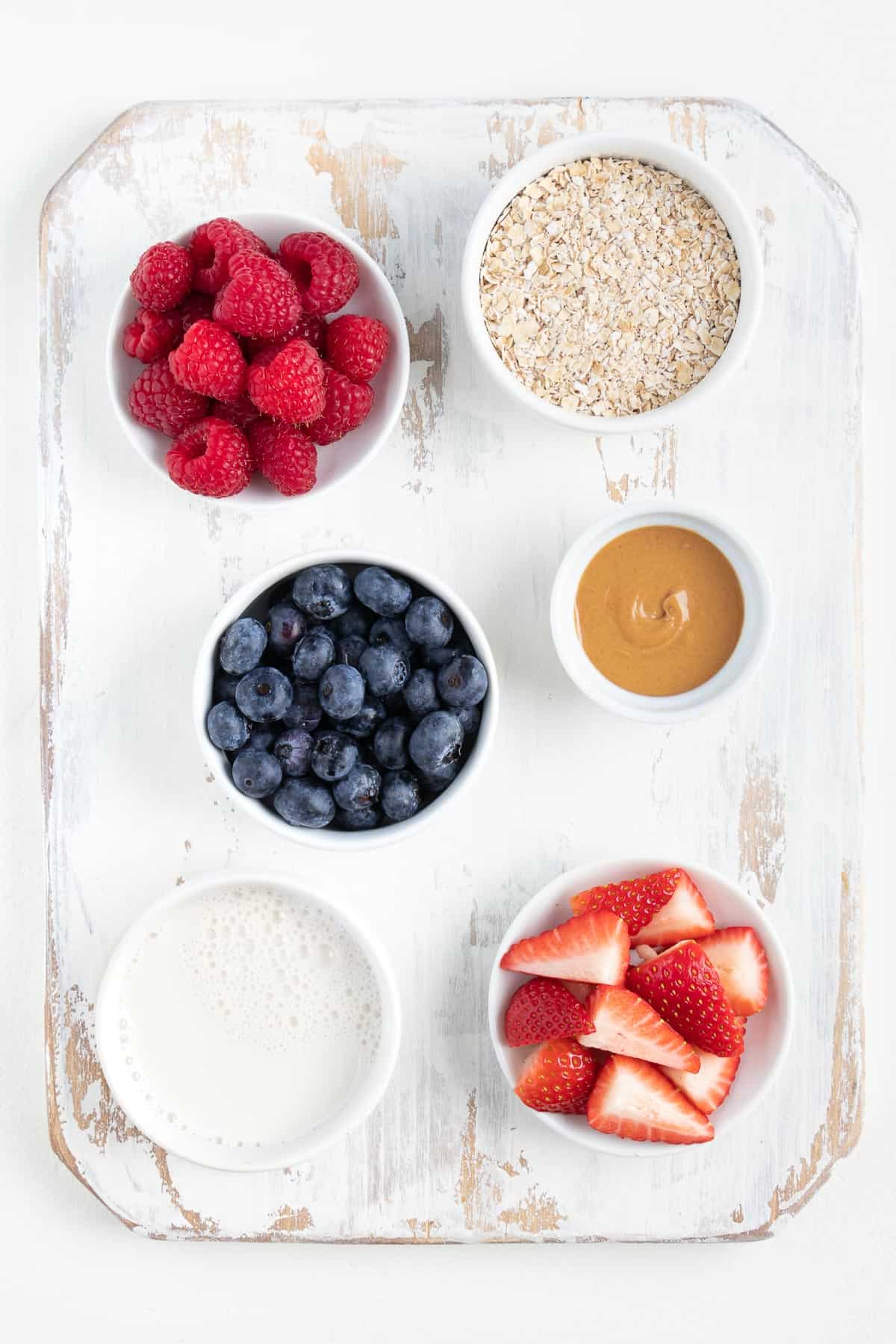 small bowls of raspberries, blueberries, strawberries, milk, oats, and peanut butter