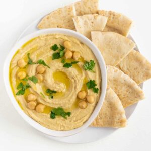 roasted garlic hummus with parsley and chickpeas on top surrounded by sliced pita bread