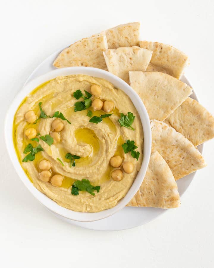 roasted garlic hummus with parsley and chickpeas on top surrounded by sliced pita bread