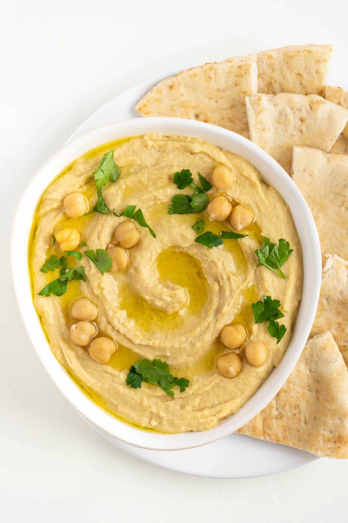 vegan roasted garlic hummus with parsley, chickpeas, and olive oil on top beside pita bread