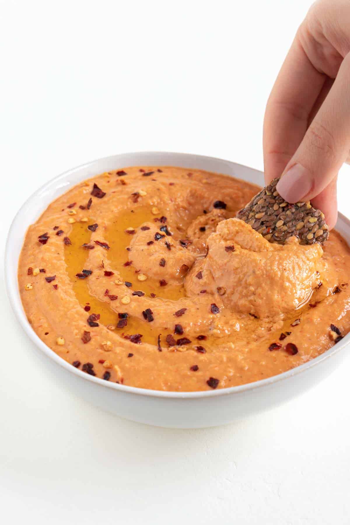 a hand dipping a cracker into hummus