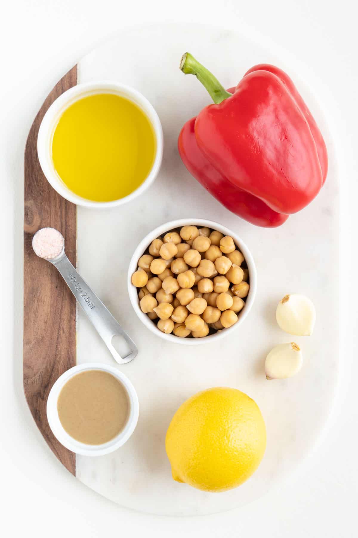 garbanzo beans, a red bell pepper, lemon, tahini, olive oil, garlic, and a teaspoon of salt on a marble white cutting board
