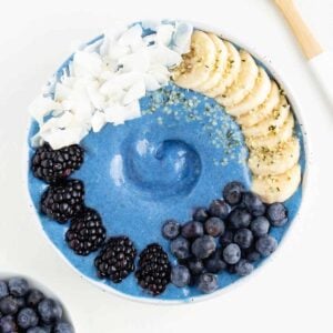 a blue smoothie bowl between a bowl of blueberries and a wooden spoon