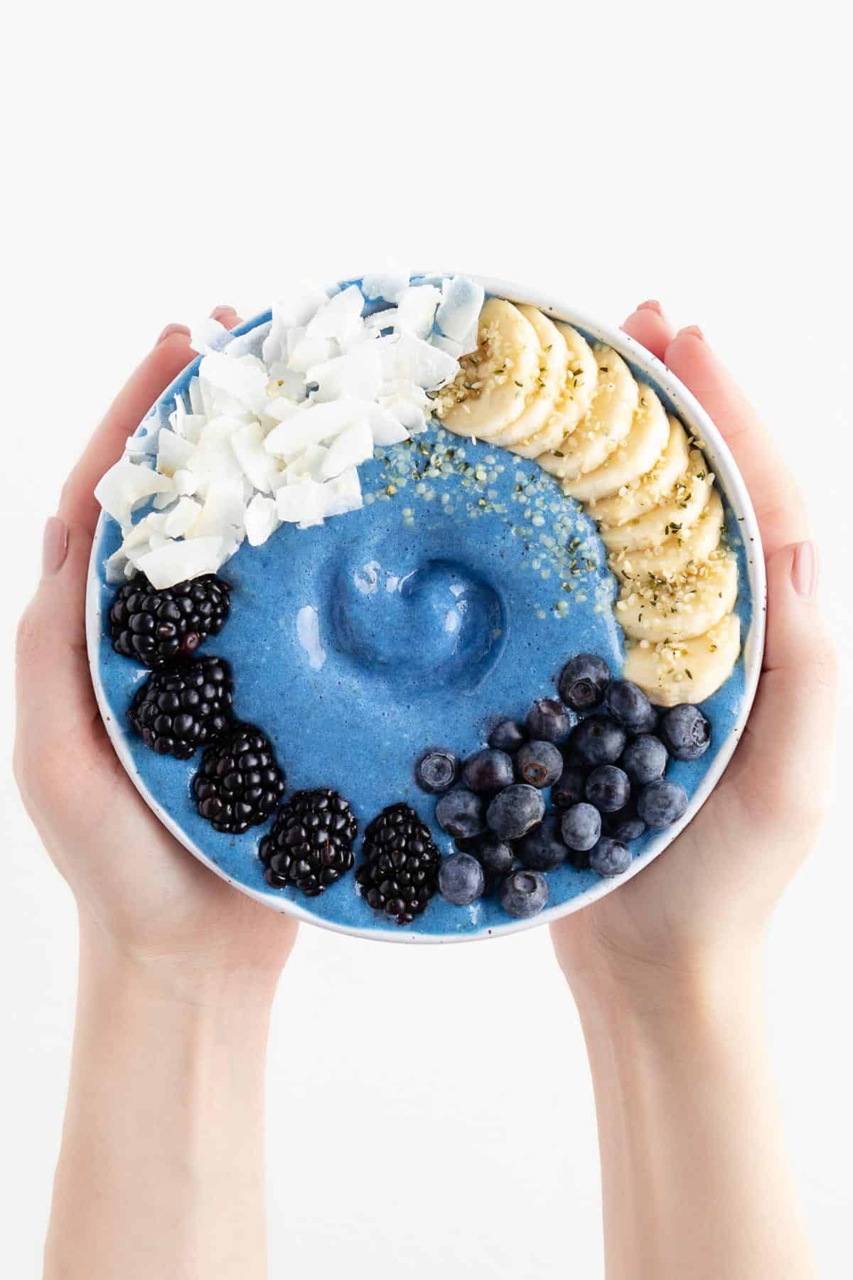 two hands holding a blue smoothie bowl