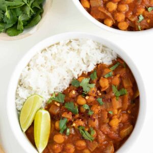 easy chickpea curry and white rice inside a bowl beside a wooden spoon and cilantro
