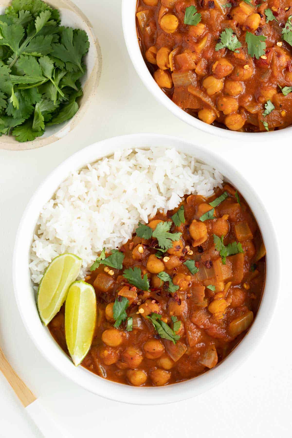 two bowls of easy chickpea curry with basmati rice beside a small bowl filled with fresh cilantro