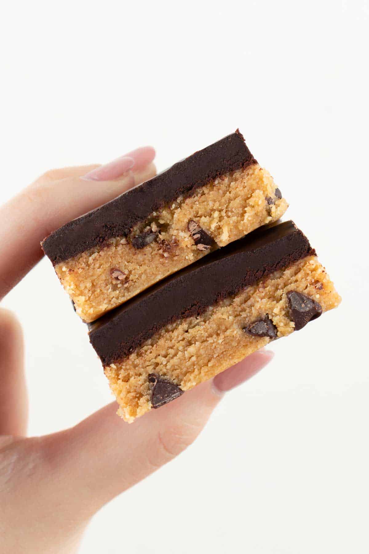 a hand holding a stack of two vegan no bake cookie dough bars