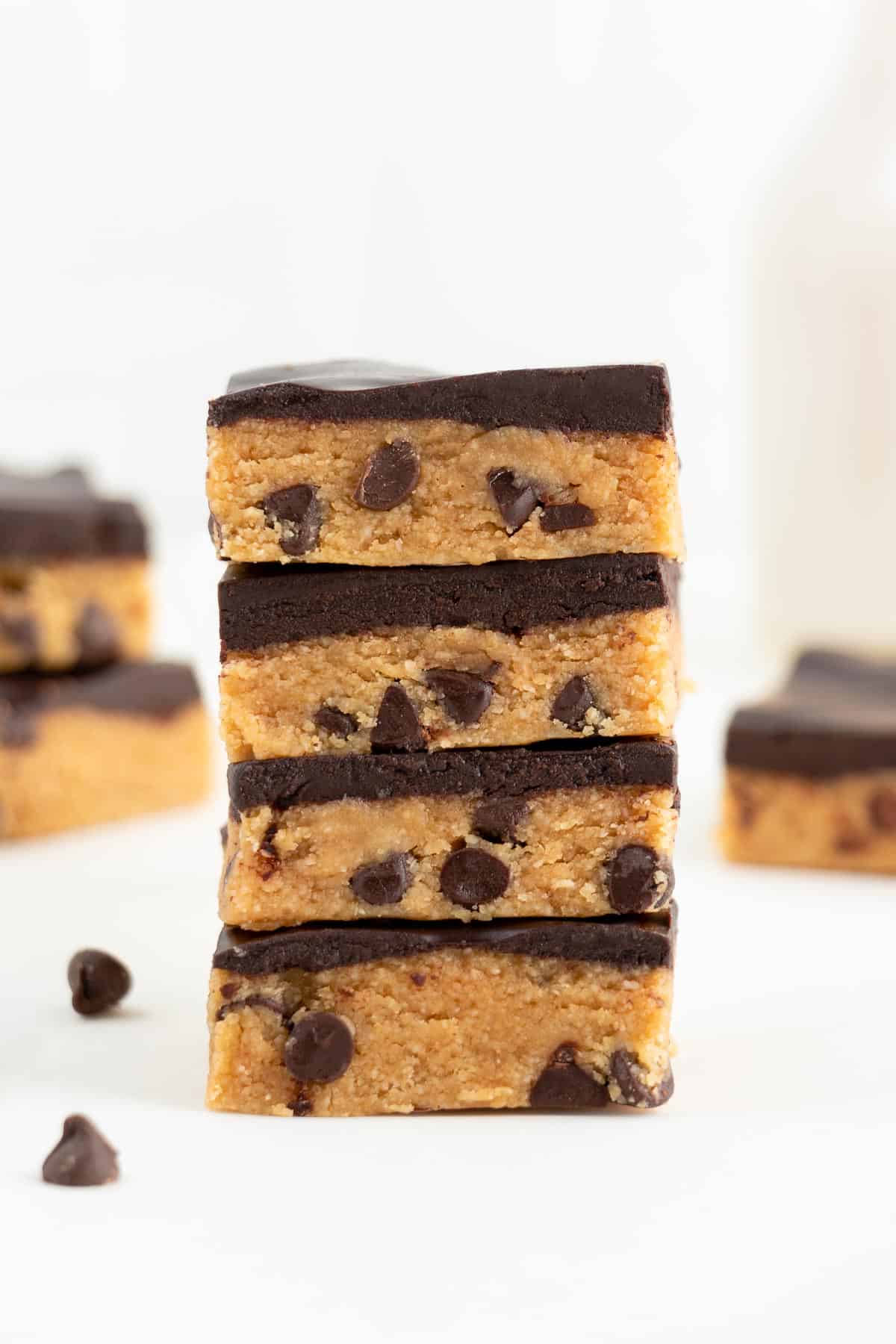 four no bake cookie dough bars stacked in front of a glass of almond milk