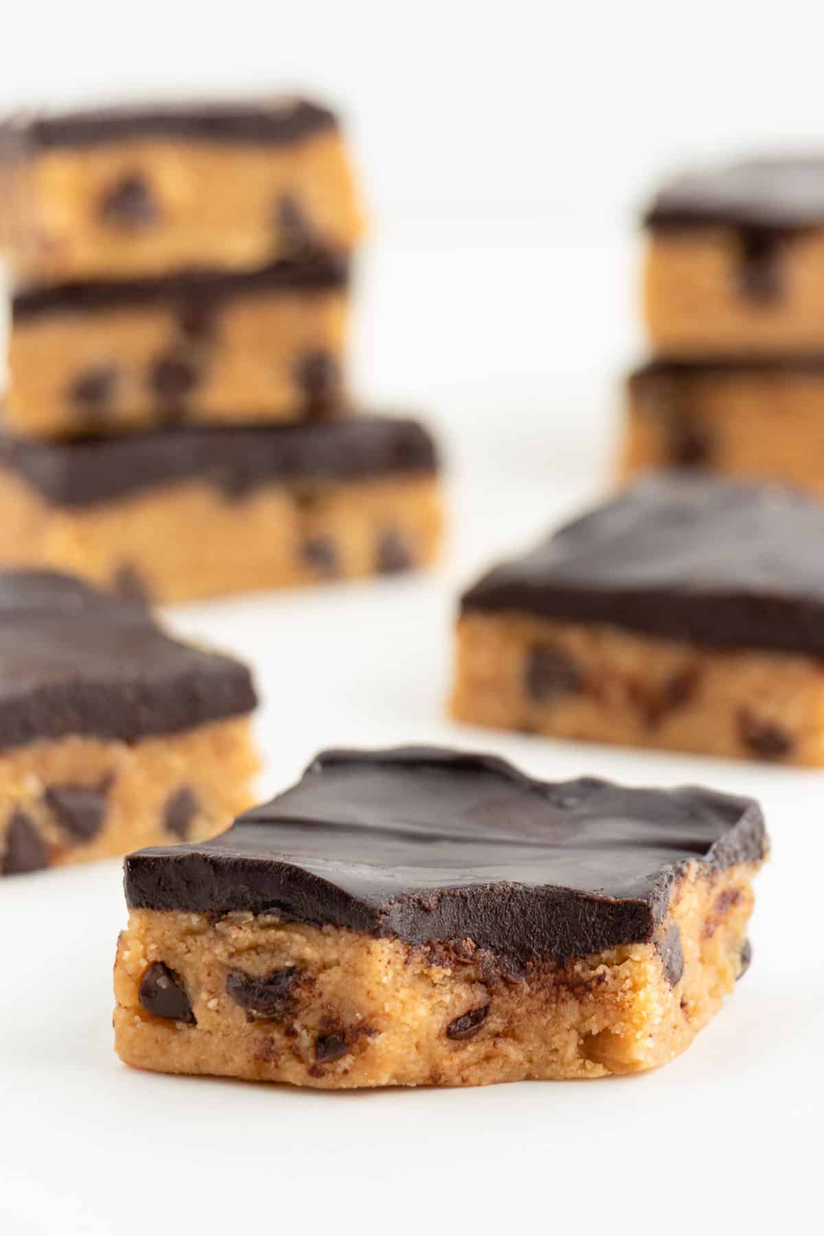a vegan cookie dough bar with a bite taken out of it and stacks of more bars behind it