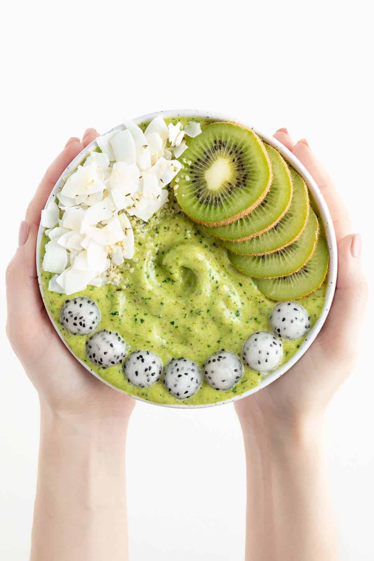 two hands holding a pineapple kale smoothie bowl