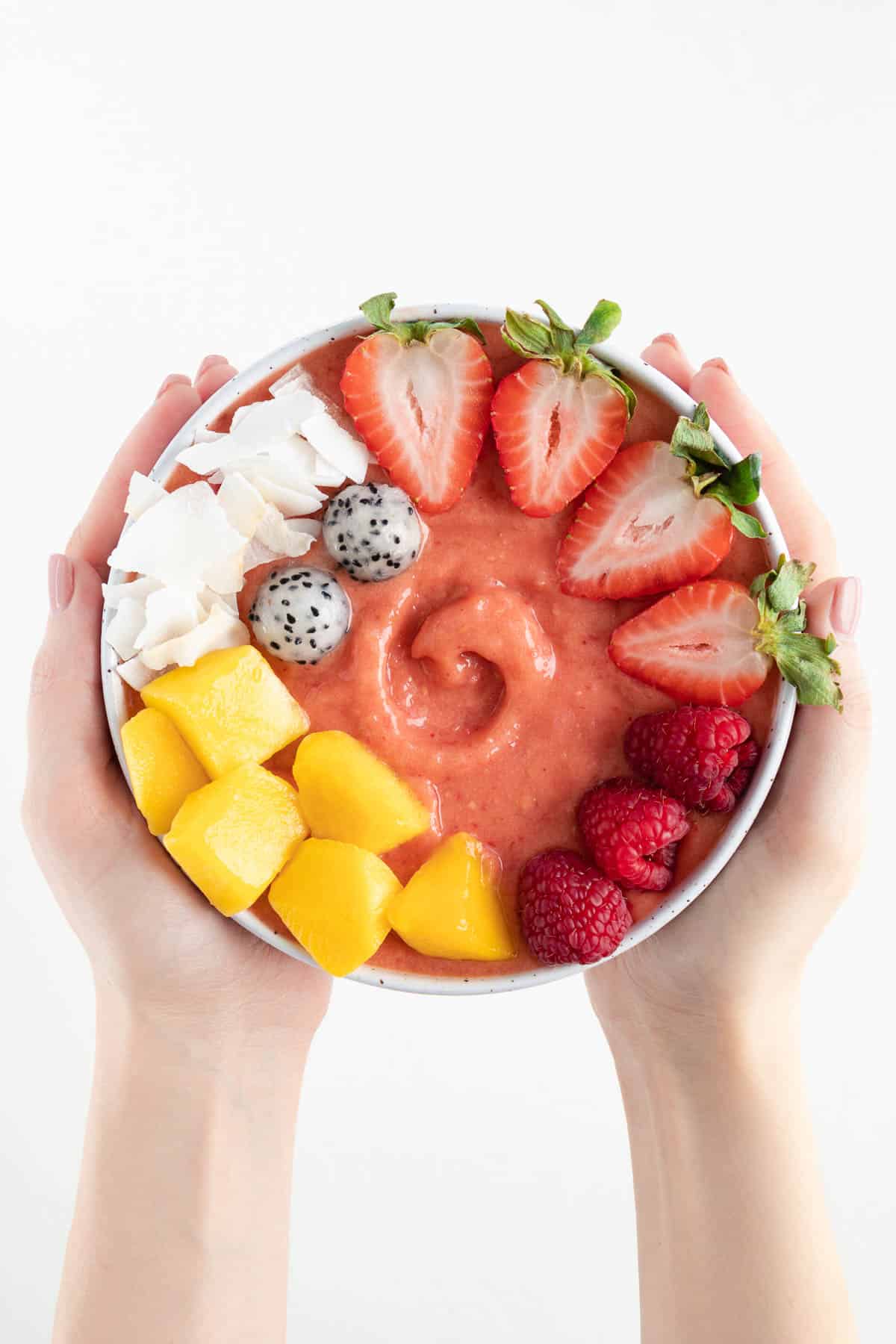 two hands holding a strawberry mango smoothie bowl