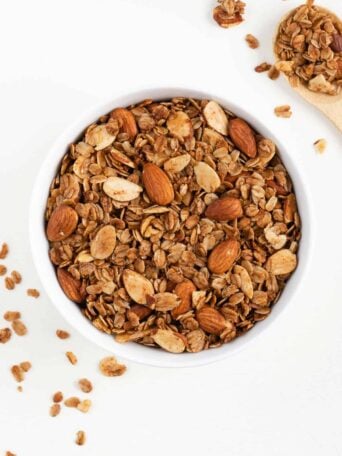 a white bowl filled with vanilla almond granola beside a wooden spoon