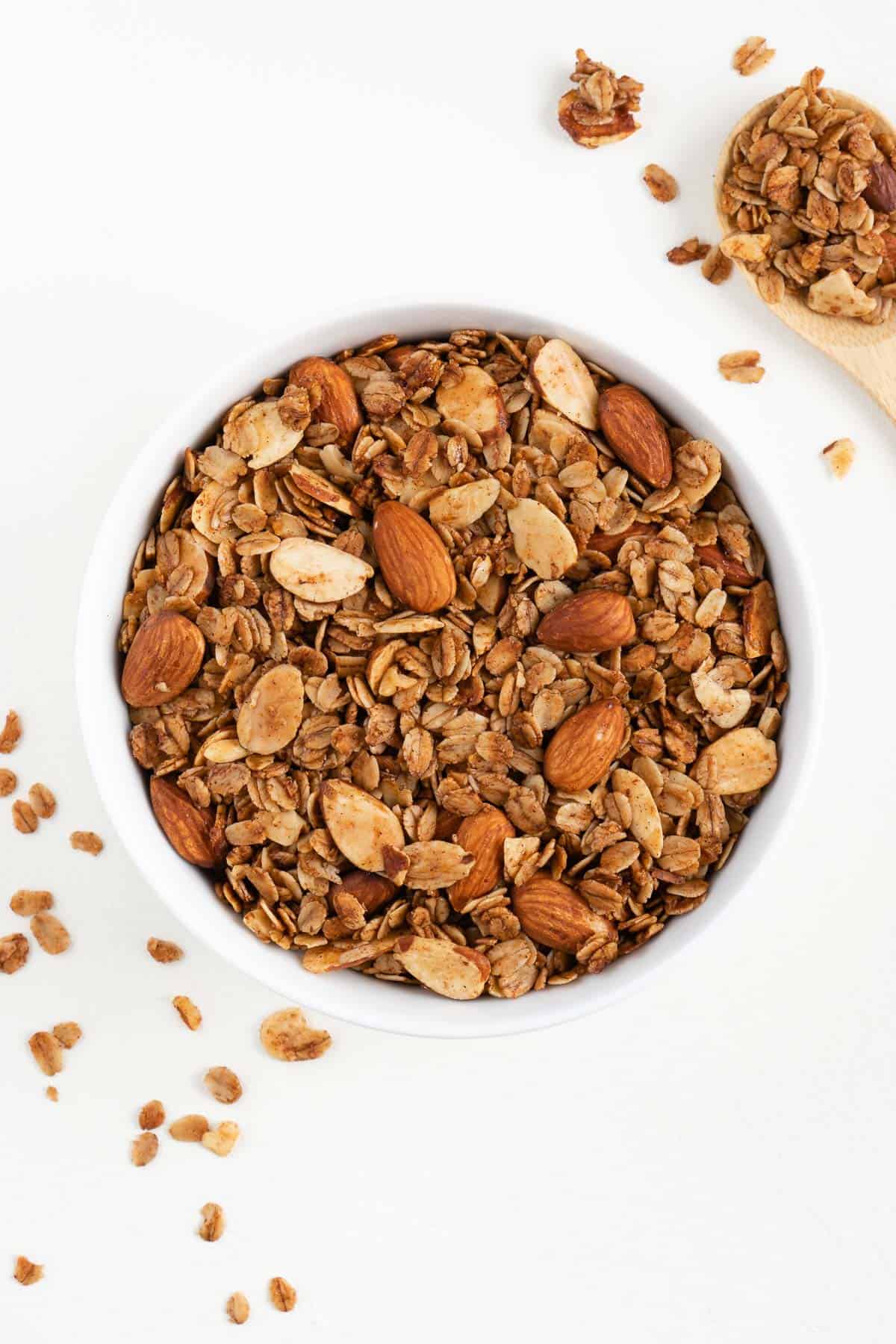 a white bowl filled with vanilla almond granola beside a wooden spoon