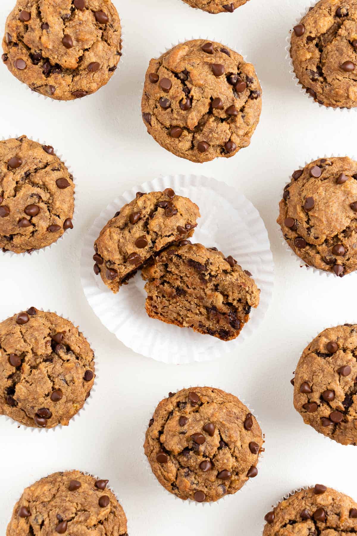 vegan banana chocolate chip muffins on a white surface with the center muffin sliced in half